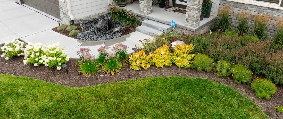 Landscape bed along grass and a walkway in Omaha, NE, with plants.