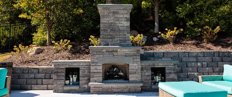 An outdoor fireplace in Omaha, NE, with a retaining wall near blue chairs.